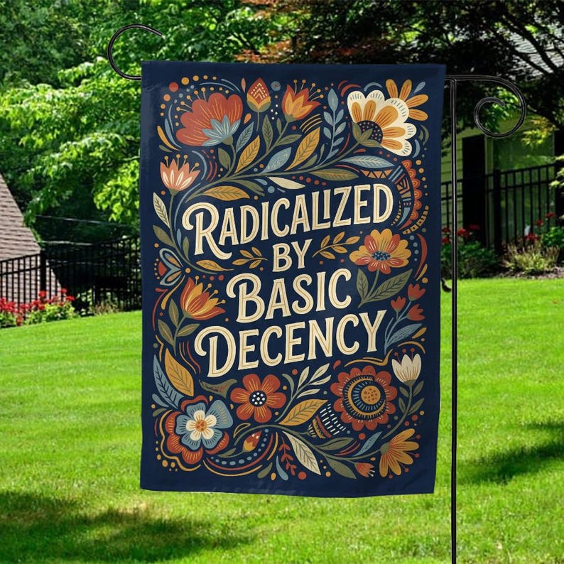 May include: A navy blue garden flag featuring the text "RADICALIZED BY BASIC DECENCY" in a decorative font. The flag is decorated with floral and leaf designs in orange, blue, and cream. It is displayed on a black metal garden stake.