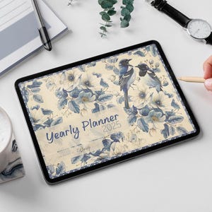 Peut inclure: Une tablette numérique affichant un agenda annuel 2025 avec un motif floral composé de fleurs bleues et blanches et d'oiseaux. Le texte "Yearly Planner 2025" est visible à l'écran.