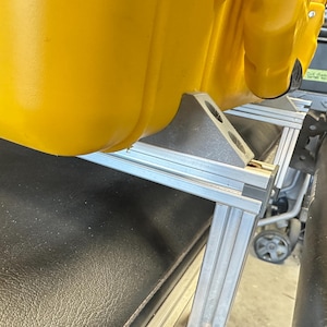 May include: A yellow plastic container with a silver metal frame and brackets. The container is sitting on a black surface.