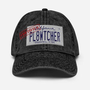 May include: Black distressed denim baseball cap with a white patch featuring a California license plate with the text "CERTIFIED" stamped over it in red. The license plate reads "PL8WTCHER" and "SESQUICENTENNIAL 150 YEARS".
