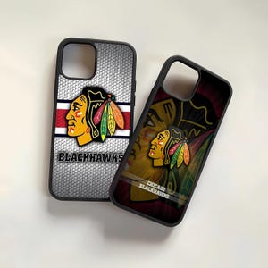May include: Two black phone cases with a Chicago Blackhawks logo. The logo features a Native American headdress with red, white, and black feathers. One case has a white background with a black grid pattern. The other case has a red, white, and black background with a faded pattern.