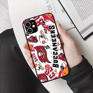 May include: A black phone case with a white background and a red, white, and black Tampa Bay Buccaneers logo design. The case features the team's name, logo, and the words "Tampa Bay" and "Buccaneers".