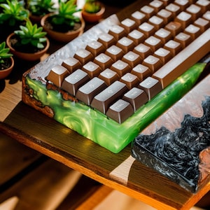 以下が含まれることがあります： 茶色のキーキャップと緑と茶色の樹脂ベースを備えたカスタムメカニカルキーボード。木製のフレームと滑らかで光沢のある仕上がりで、ユニークなデザインです。小さな鉢植えの多肉植物が背景にあります。