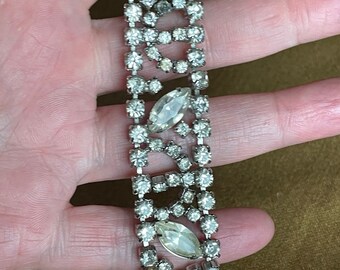 May include: A silver tone rhinestone bracelet with a repeating pattern of marquise and round rhinestones.