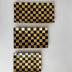 May include: Three rectangular trays arranged vertically, each featuring a repeating checkerboard pattern of alternating black squares and shimmering gold-toned squares. The trays vary in size, with the largest at the top and the smallest at the bottom.