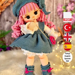 Peut inclure: Poupée au crochet avec des cheveux roses bouclés, vêtue d'une robe, d'un chapeau et de bottes bleus avec des accents roses. La poupée a un petit sac à main rose. Le texte dit "PDF PATTERN ONLY - NOT FINISHED DOLL."