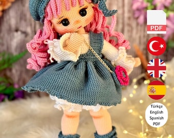 Puede incluir: Muñeca de ganchillo con cabello rizado rosa, vestida con un vestido azul, sombrero y botas con detalles en rosa. La muñeca tiene un pequeño bolso rosa. El texto dice "PDF PATTERN ONLY - NOT FINISHED DOLL."