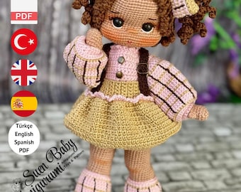 May include: A crochet doll with brown curly hair, wearing a pink and beige dress, shoes, and a headband. The doll has a backpack. The image includes text that says "Suen Baby Amigurumi" and "PDF PATTERN ONLY - NOT FINISHED DOLL."