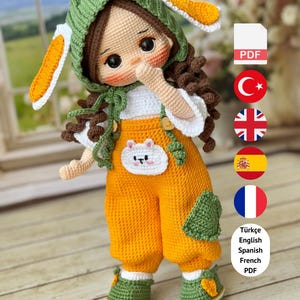 May include: A handmade crochet doll wearing an orange jumpsuit, green shoes, and a green bunny hat with white and orange accents. The doll has brown curly hair and a white shirt. The text "PDF PATTERN ONLY - NOT FINISHED DOLL" is at the bottom.