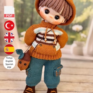 Puede incluir: Muñeca de ganchillo hecha a mano con un suéter con capucha naranja, pantalones azules y zapatos marrones. La muñeca tiene una pequeña bolsa marrón y un peinado marrón y beige. La cara de la muñeca tiene grandes ojos negros. El texto dice "PDF PATTERN ONLY - NOT FINISHED DOLL."