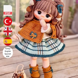 Puede incluir: Muñeca de ganchillo con coletas marrones, que lleva una capa color mostaza y una falda a cuadros azul y verde. La muñeca tiene botas marrones y un pequeño bolso. El texto "PDF PATTERN ONLY - NOT FINISHED DOLL" es visible.