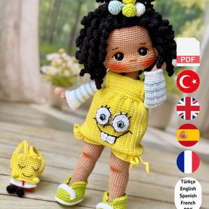 Puede incluir: Una muñeca de ganchillo hecha a mano con cabello negro rizado, que lleva un vestido amarillo con una cara de dibujos animados. La muñeca tiene zapatos verdes y un pequeño accesorio a juego. La imagen incluye texto: PDF PATTERN ONLY - NOT FINISHED DOLL.