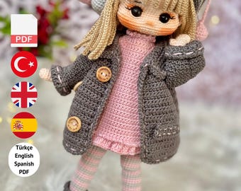 May include: A handmade crochet doll wearing a gray coat, hat, and boots, with a pink dress and striped leggings. The doll has blonde hair and a sweet expression. The image includes text that says "PDF PATTERN ONLY - NOT FINISHED DOLL."