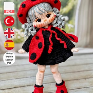 Peut inclure: Poupée crochetée faite à la main, vêtue d'un costume de coccinelle, avec un chapeau rouge à pois noirs, une robe noire et des bottes rouges. La poupée a des cheveux gris et une expression douce. Le texte indique un patron PDF.