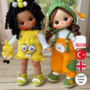 May include: Two handmade crochet dolls. One doll wears a yellow dress with a cartoon face, green shoes, and holds a matching toy. The other doll wears orange overalls, a green hat with bunny ears, and green shoes. The dolls are displayed in front of a window.