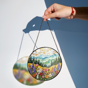 a hand is holding a circular painting hanging from a chain