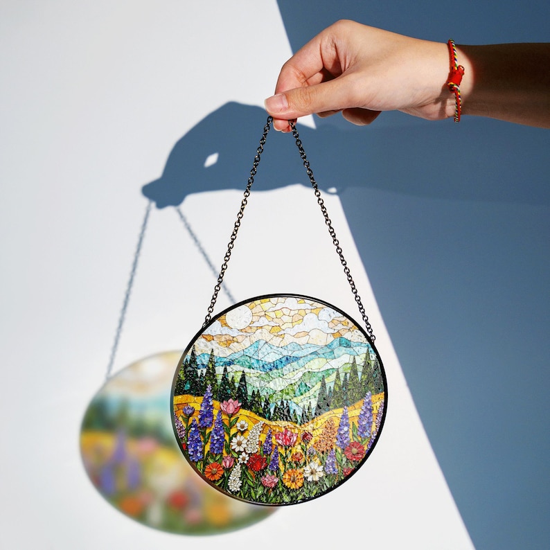 a hand is holding a circular painting hanging from a chain