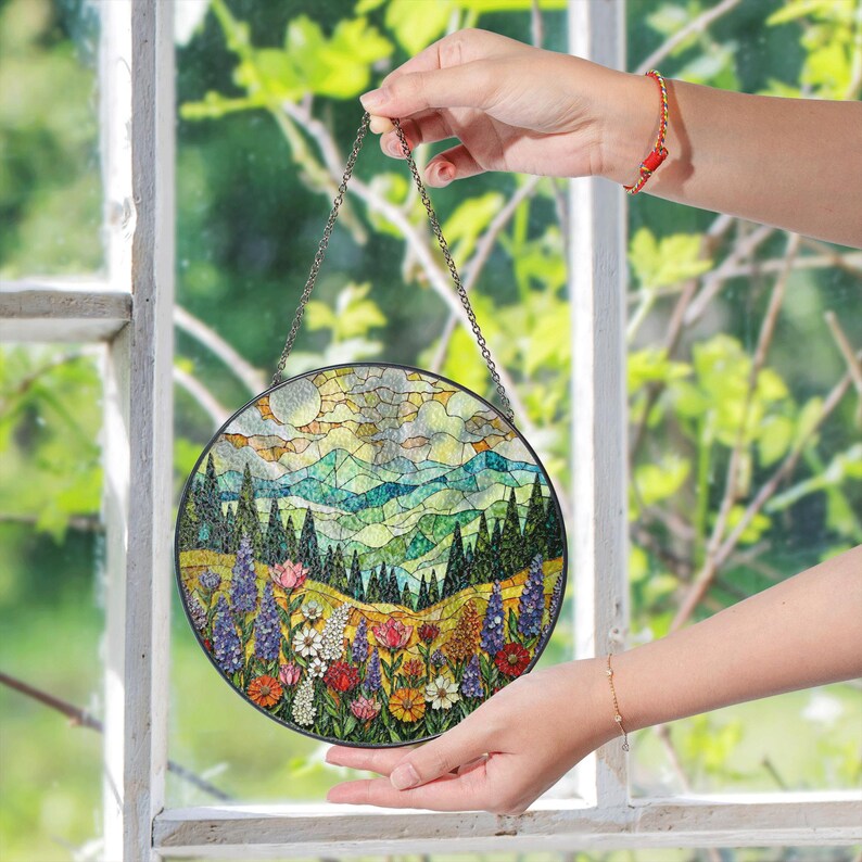 a person holding a stained glass window with a view of a mountain