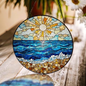 May include: A round stained glass window depicting a seascape with a bright yellow sun, blue waves, and a sandy beach.