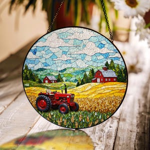 May include: A stained glass window hanging depicts a red tractor in a field of wheat with a red barn in the background. The sky is blue with white clouds.
