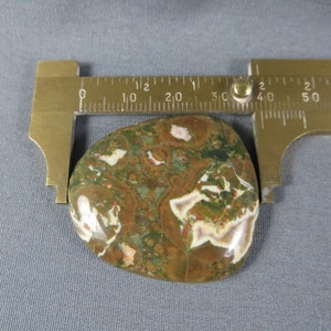 May include: A green, brown, and white agate cabochon with a swirling pattern. The cabochon is approximately 2 inches long and 1.5 inches wide.