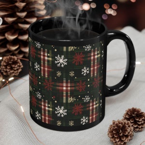Könnte beinhalten: Schwarze Keramiktasse mit rotem und grünem Karomuster und weißen Schneeflocken. Die Tasse ist mit Kaffee gefüllt und Dampf steigt aus der Oberseite auf.