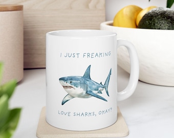 May include: White ceramic mug with a blue and white illustration of a shark and the text "I just freaking love sharks, okay?"