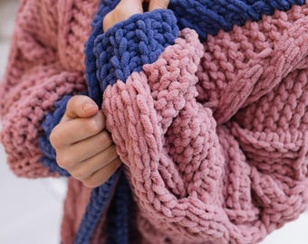 May include: A pink and blue knitted cardigan with a chunky knit texture. The cardigan has a long sleeve and a loose fit.