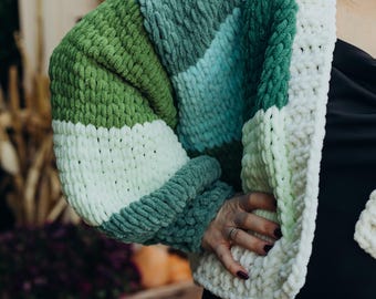 May include: A chunky knit cardigan with stripes of green, white, and blue. The cardigan is made of a soft, fuzzy yarn.