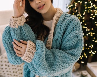 May include: A blue and cream knitted cardigan with a cable knit pattern. The cardigan is open at the front and has a relaxed fit.