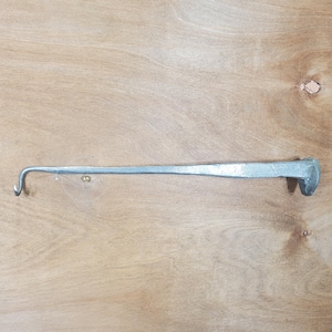 May include: A silver-coloured, long, metal tool with a curved hook on one end and a wider, flattened head on the other. The tool is set against a light brown wooden surface.