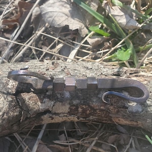 以下が含まれることがあります： ユニークなデザインのハンドメイドメタル製ボトルオープナー。オープナーは、湾曲したハンドルに取り付けられた一連の小さな正方形の金属片を特徴としています。