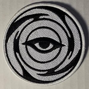 Peut inclure: Un patch circulaire blanc avec une broderie noire d'un œil stylisé à l'intérieur d'un motif tourbillonnant.