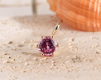 May include: A gold pendant featuring a round, faceted pink gemstone held by six prongs. The pendant includes a small gold bail at the top for attachment to a chain. The setting is polished yellow gold, showcasing a vibrant, deep pink stone.