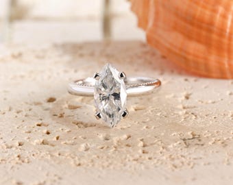 May include: A silver-toned ring featuring a central marquise-cut clear gemstone held by four prongs. The band has a smooth, polished finish with subtle beaded detailing along the shoulders, creating a refined and classic appearance for the jewelry.