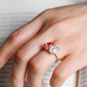 May include: A ring with a pear-shaped pink gemstone and a square-shaped clear gemstone set in a gold band.