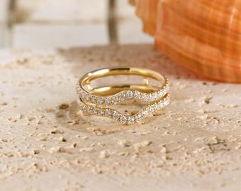 May include: A gold ring guard featuring a curved, open design with two parallel bands. Each band is encrusted with a row of small, clear, round-cut stones that follow the wavy contour of the metal, creating a continuous sparkling effect.