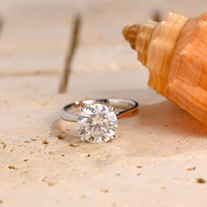 Puede incluir: Un anillo de compromiso de plata con un gran diamante redondo y claro.