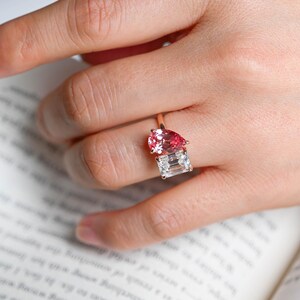 May include: A ring with a pear-shaped pink gemstone and a square-shaped clear gemstone set in a gold band.