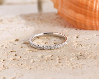 May include: A thin silver-toned band ring featuring a continuous row of small, clear, sparkling stones set along the outer circumference. The metal has a polished, reflective finish, and the stones are arranged in a uniform, circular pattern.