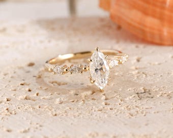 May include: A gold ring featuring a central marquise-cut clear gemstone held by prongs, flanked by two smaller marquise-cut clear stones on each side of the thin, polished gold band, creating a delicate and symmetrical arrangement of stones.