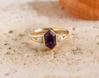 May include: A gold ring featuring a central hexagonal purple gemstone flanked by two small white pearls. The band is crafted from a polished yellow metal, and the setting holds the stones in a secure, symmetrical arrangement on the ring shank.