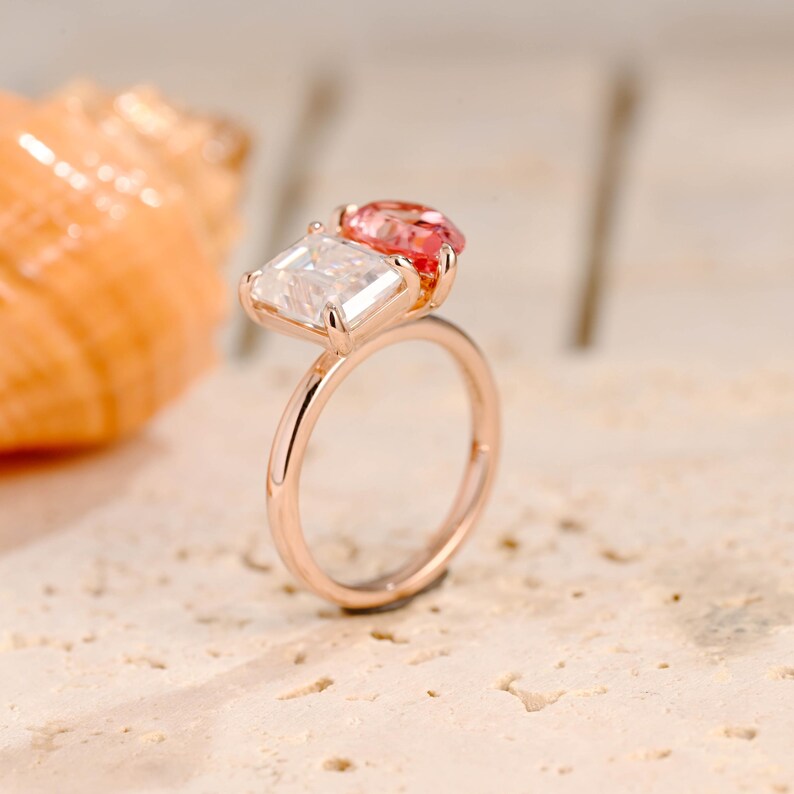 May include: A rose gold ring with two gemstones. The larger gemstone is a square-shaped, clear stone. The smaller gemstone is a round, pink stone.