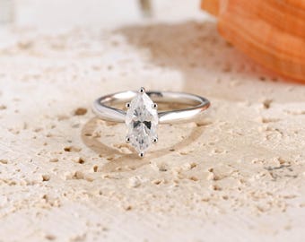 May include: A silver-toned ring featuring a single marquise-cut clear gemstone set in a six-prong setting. The band is smooth and polished, tapering slightly toward the center stone, which is positioned vertically to highlight its elongated shape.