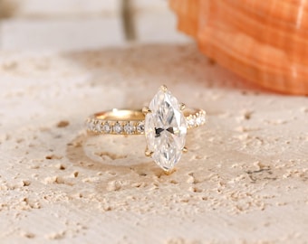 May include: A gold ring featuring a large marquise-cut center stone and a band accented with small round pavé-set stones. The metal band has a polished finish, and the central gemstone is held in place by a multi-prong setting for secure placement.