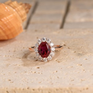 Può includere: Un anello in oro rosa con un grande rubino ovale circondato da un'aureola di diamanti più piccoli.