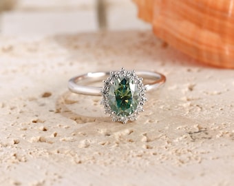 May include: A silver-toned ring featuring an oval-cut teal gemstone at the center, surrounded by a halo of small, clear, round-cut stones. The band is smooth and metallic, providing a clean contrast to the intricate, sparkling stone setting.