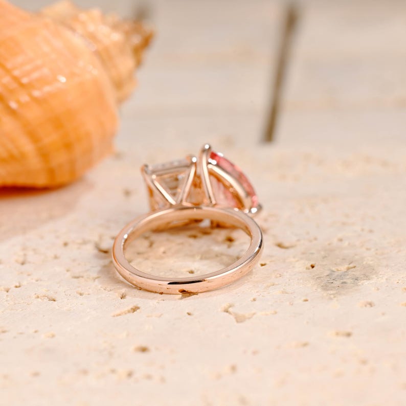 May include: A rose gold engagement ring with a large, square-cut center stone and a smaller, round-cut stone on the side. The ring is set on a simple band.