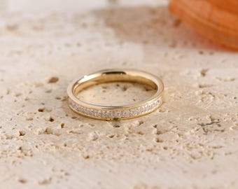 May include: A gold band ring featuring a channel setting with a continuous row of small, clear, square-cut stones embedded along the center of the outer surface. The metal has a polished finish, and the stones are set flush within the band.
