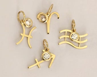 May include: Four gold-toned metal zodiac charms, each featuring a small circular clear gemstone set at the top. The charms represent the Pisces, Aries, Aquarius, and Sagittarius symbols, and each includes a small jump ring for attachment to jewelry.